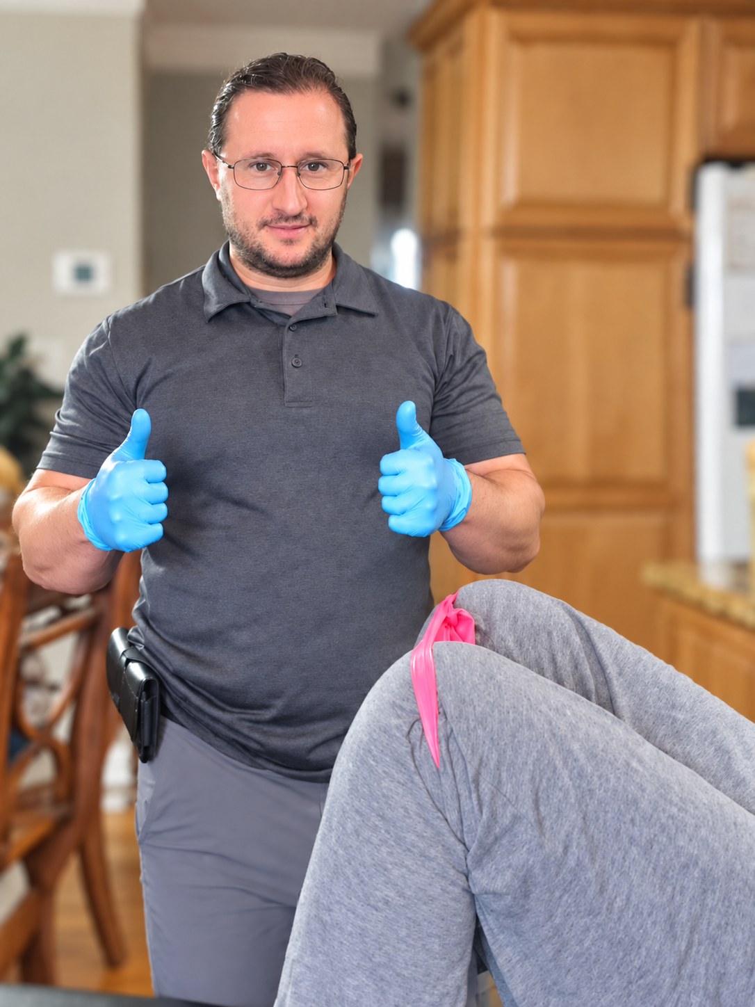 Dr. Lenny Klichinsky smiles during an in-home exercise visit; a pink resistance band is visible near the client’s legs